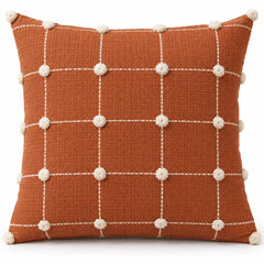 Rust orange square cushion cover with white grid lines and pom-pom details at the grid intersections