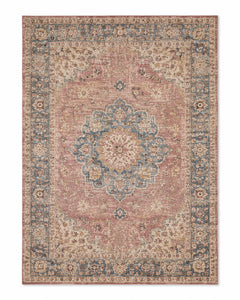 Softly distressed Persian-inspired area rug with dusty pink field, blue floral medallion and border, and warm beige accents