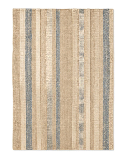 Beige and dusty blue handwoven area rug with varied artisan-style vertical stripes on a white background.