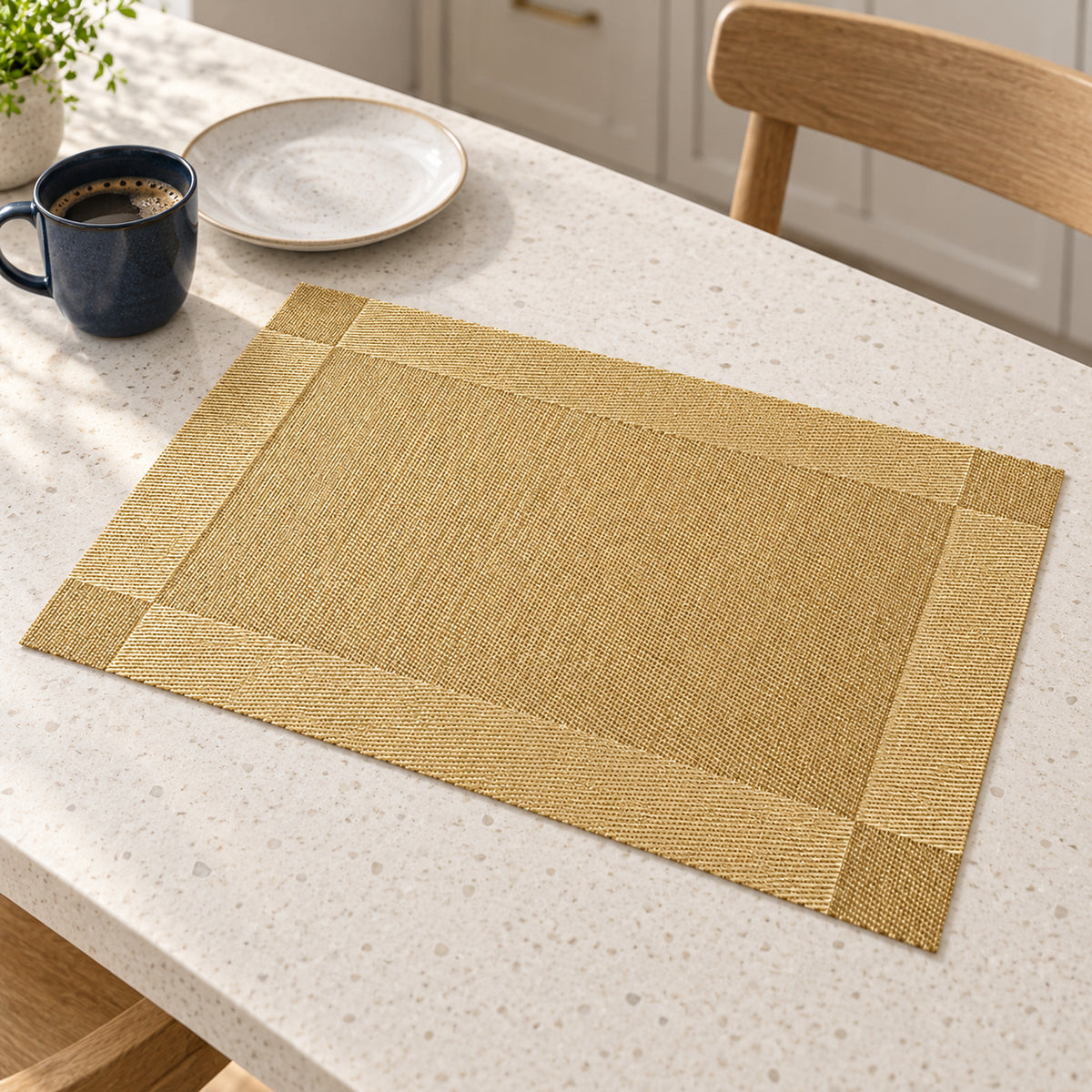 Sand beige rectangular table placemat with a wide champagne gold border resting on a cream speckled kitchen counter