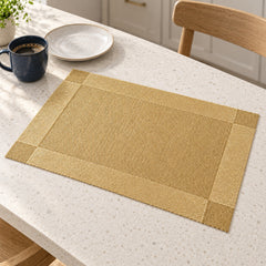 Sand beige rectangular table placemat with a wide champagne gold border resting on a cream speckled kitchen counter