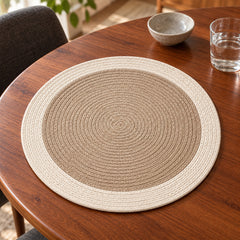 Round taupe-beige dining placemat with tightly coiled concentric rings and a contrasting ivory outer band on a walnut wooden table