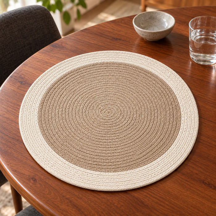 Round taupe-beige dining placemat with tightly coiled concentric rings and a contrasting ivory outer band on a walnut wooden table