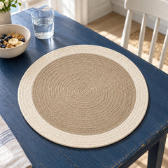 Round oat beige placemat showing tightly concentric rope-like spiral rings and a wide ivory outer border on a navy blue tabletop