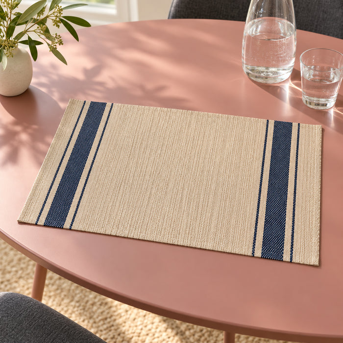 Beige rectangular table placemat with narrow and broad navy blue stripes down both ends, displayed on a muted pink dining table