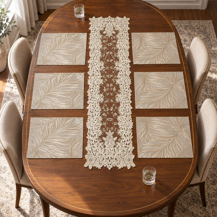 Styled dining table with six ivory botanical leaf-pattern placemats and a long ivory floral lace-look table runner at the centre