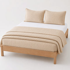 Beige seersucker stripe cotton quilt, folded with matching pillows for wholesale bedding sourcing