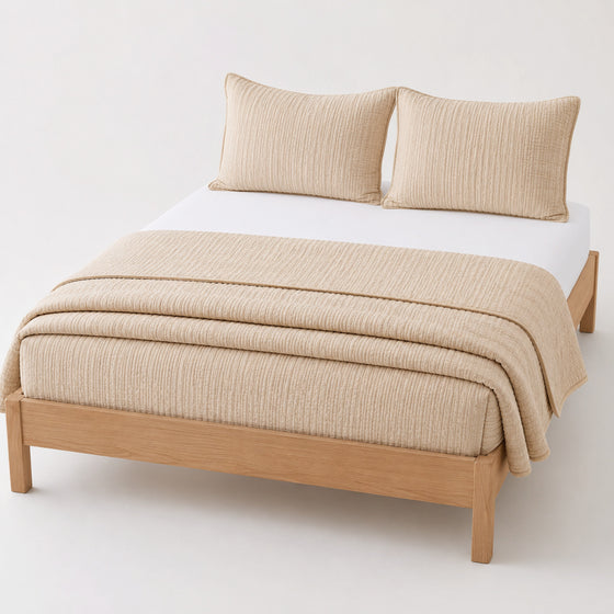 Beige seersucker stripe cotton quilt, folded with matching pillows for wholesale bedding sourcing