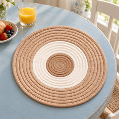 Round beige and ivory placemat with concentric rope-like rings on a pale blue dining table