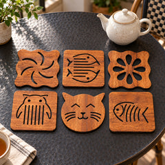 Set of six warm brown wood-look coasters with varied decorative cutout motifs including a cat face, fish, owl and flower on a black stone table