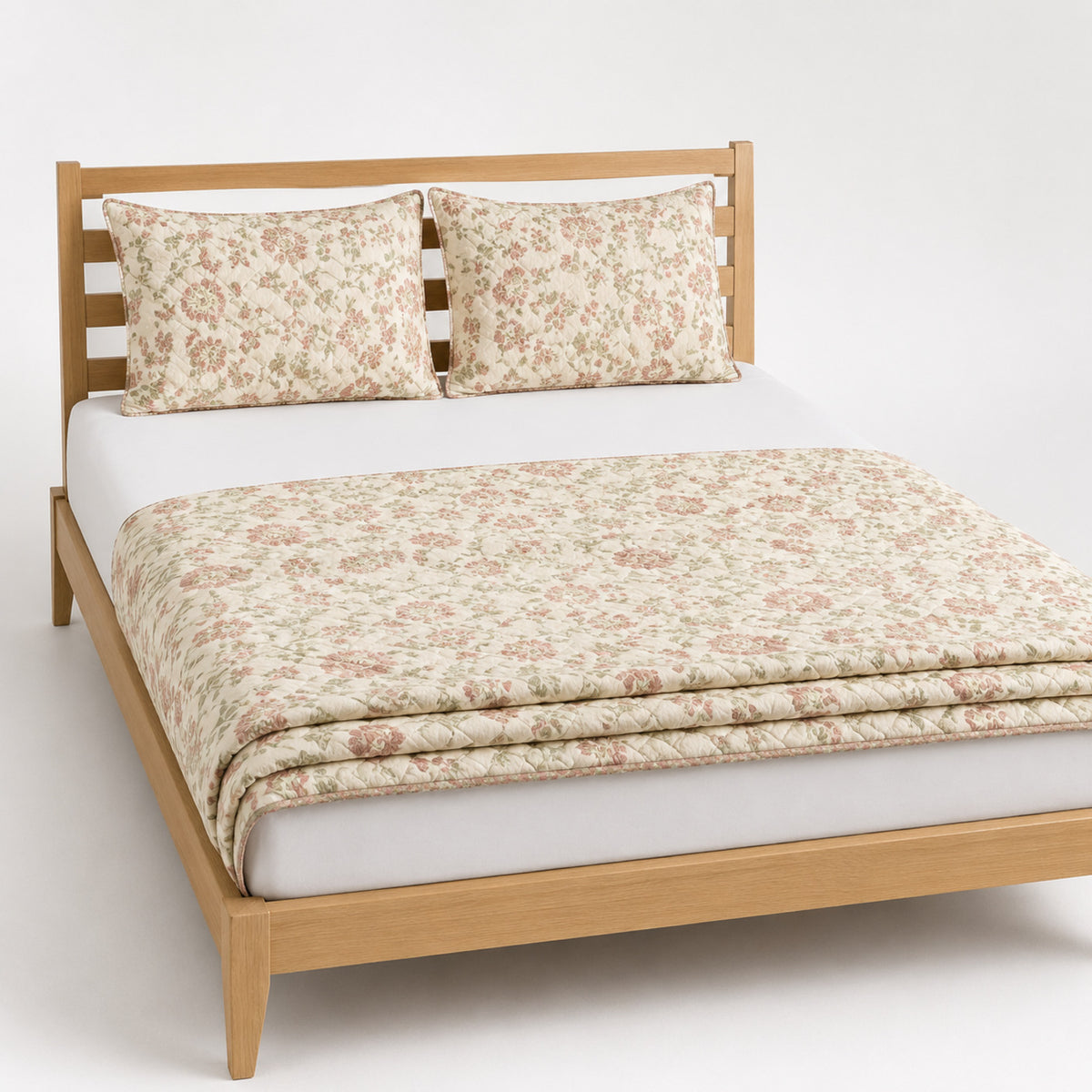 Cream muted rose and sage floral cotton quilt, folded with matching pillows for wholesale bedding sourcing