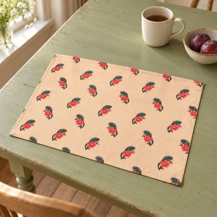 Cream rectangular placemat printed with scattered tiny red rosebuds and muted green leaves on a sage-painted wooden dining table