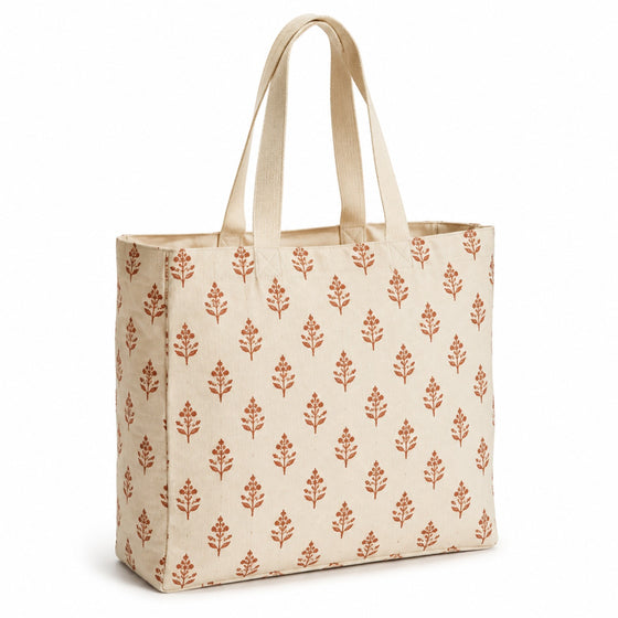 Cream tote bag with terracotta block-printed leaf motifs and natural handles on a white background.