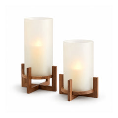 Two opaque ivory frosted-glass cylindrical candle holders in different heights on crossed dark honey-wood support bases