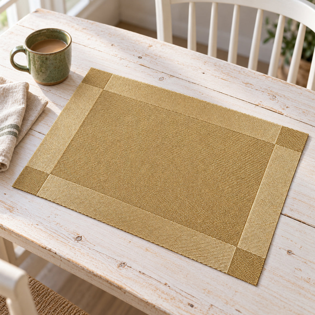 Neutral beige rectangular woven-look placemat with a broad gold border on a light table