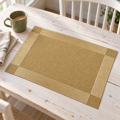 Neutral beige rectangular woven-look placemat with a broad gold border on a light table
