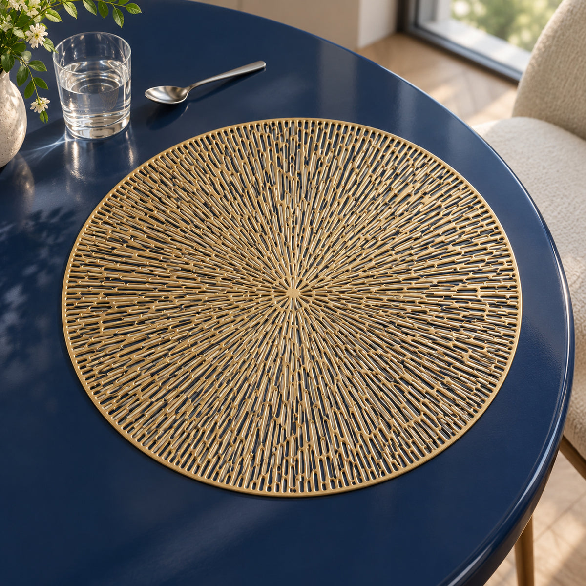 Round golden sunburst placemat with fine radiating filigree-style spokes and a circular border on a dark navy dining table