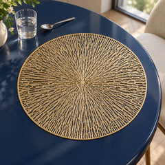 Round golden sunburst placemat with fine radiating filigree-style spokes and a circular border on a dark navy dining table