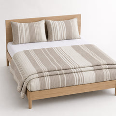 Greige and ivory linear cotton quilt, folded with matching pillows for wholesale bedding sourcing