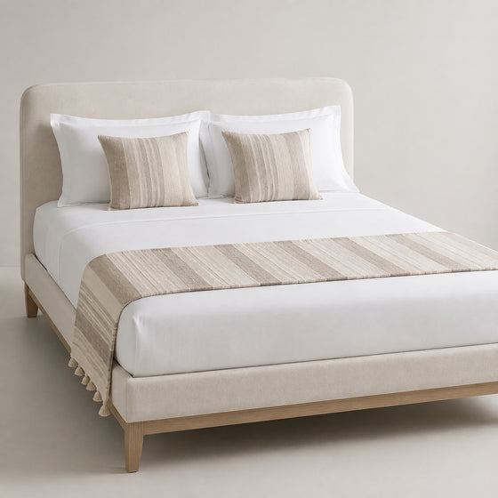 Greige wide-stripe bed runner with subtle fringe, styled on white bedding for wholesale hospitality and private-label sourcing