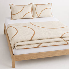 Ivory and caramel curved contemporary cotton quilt, folded with matching pillows for wholesale bedding sourcing