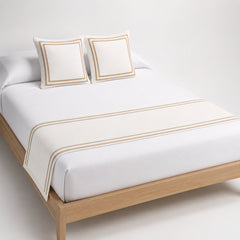 Ivory bed runner with refined double stripe border, styled on white bedding for wholesale hotel and home textile sourcing