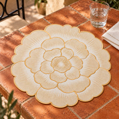 Ivory flower-shaped dining placemat with layered rounded scalloped petals and fine gold-coloured outlines on a terracotta tiled table