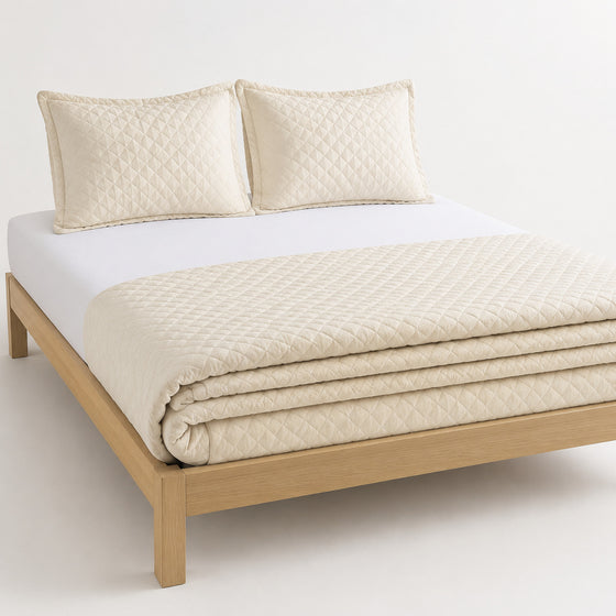 Ivory tonal diamond boutique-style cotton quilt, folded with matching pillows for wholesale bedding sourcing