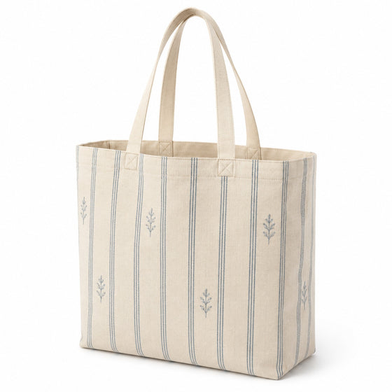 Natural tote bag with dusty blue vertical stripes and small botanical motifs on a white background.
