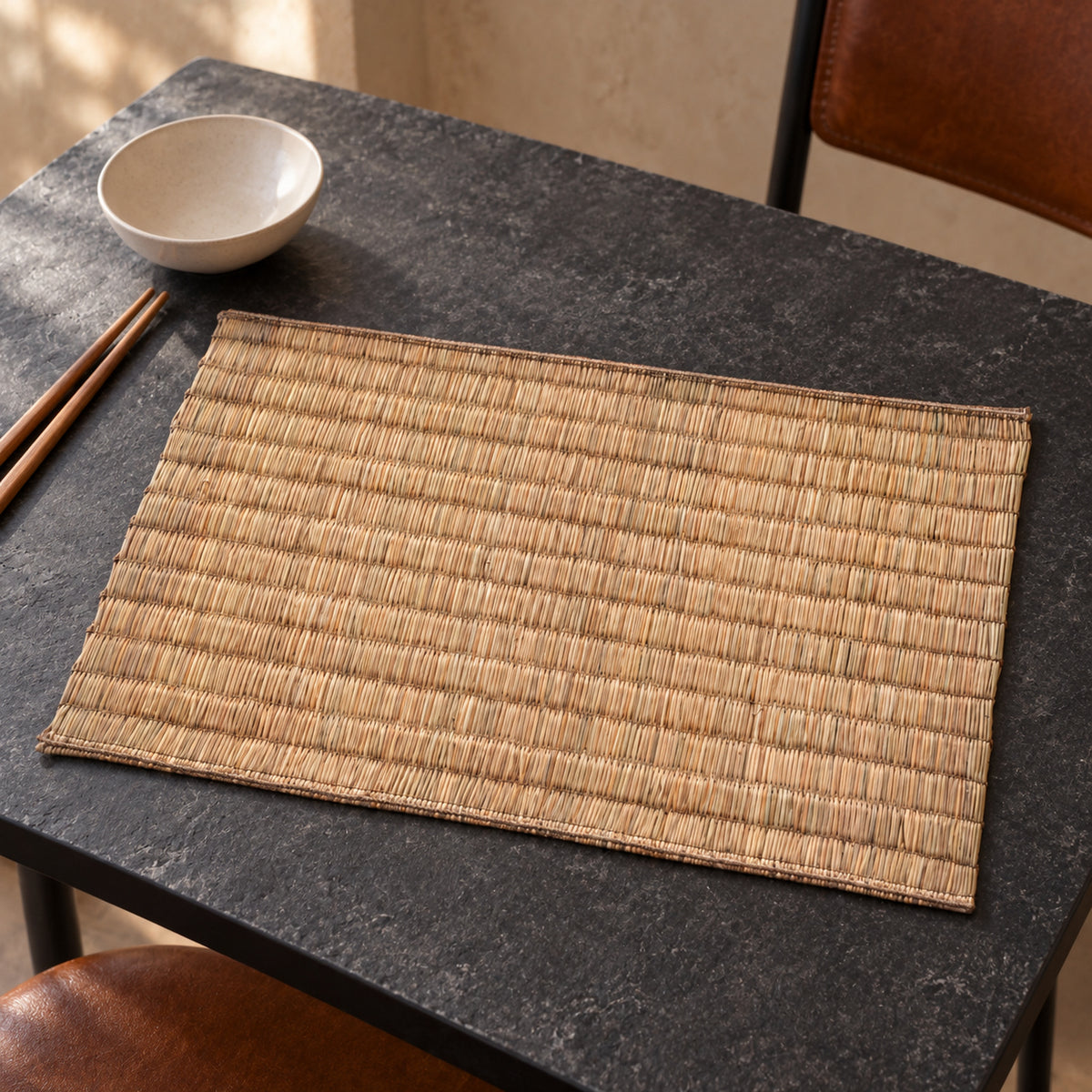Natural tan rectangular placemat with rustic woven-look horizontal strips and darker border on a black dining table