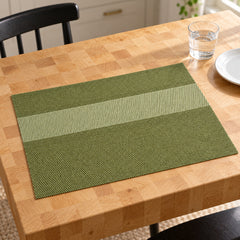 Rectangular olive green placemat with light sage broad horizontal centre stripe and darker moss green bands on a pale wood dining table