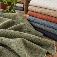 Dyed olive green cotton slub fabric with irregular woven texture beside a stack of coordinating colour swatches; Primeval fabric reference PML-FAB-009