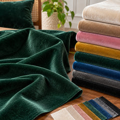 Emerald green velvet upholstery fabric draped in plush folds beside a range of velvet colour swatches; Primeval fabric sourcing reference PML-FAB-014