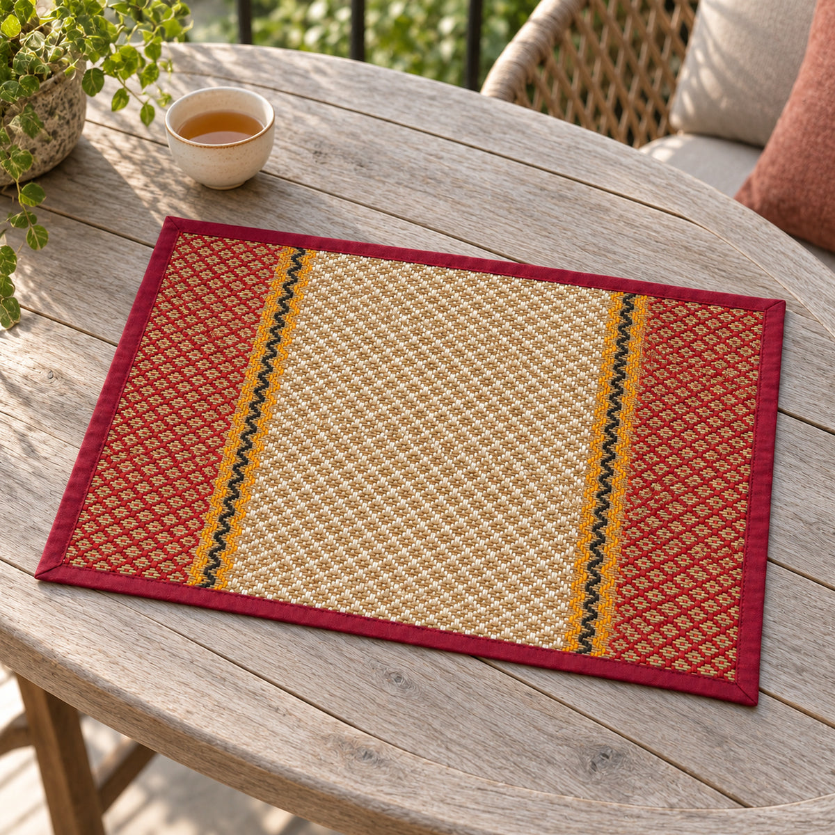 Rectangular dining placemat with red geometric side borders, golden ochre bands and a cream small diamond-pattern centre on a rustic wooden table