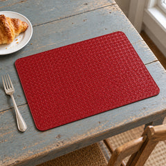 Solid deep red rectangular placemat with finely textured woven-look surface on a grey wooden dining table