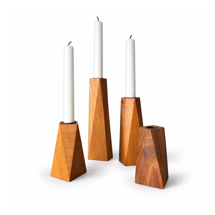 Four tapered geometric wooden candle holders in warm natural tones, three pictured with slim white taper candles