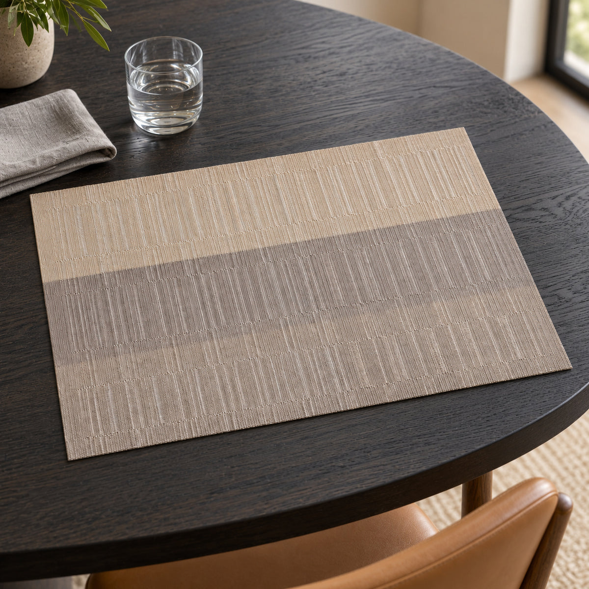 Rectangular taupe and greige placemat with delicate vertical woven-look line texture and broad tonal bands on a dark round dining table