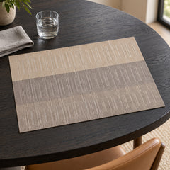 Rectangular taupe and greige placemat with delicate vertical woven-look line texture and broad tonal bands on a dark round dining table