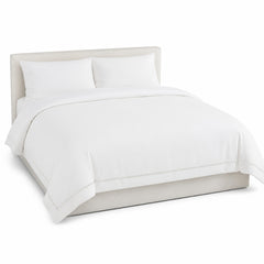 Primeval warm white decorative border duvet cover displayed on a styled bed against a clean white studio background