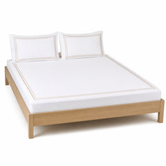 White bed sheet set with beige hotel-style border and matching pillowcases on a wooden bed