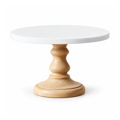 Round white cake display plate on an ornate turned light-wood pedestal with curved contours and wide circular foot